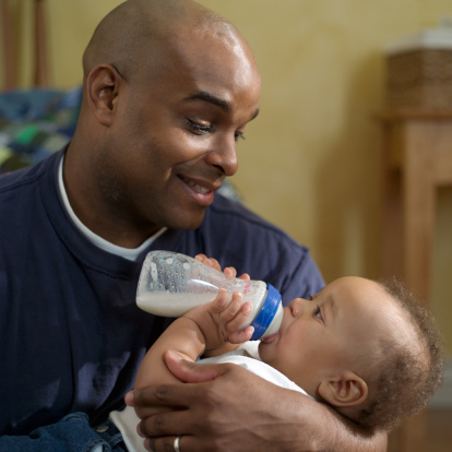 a young father feeds his new son with a bottle