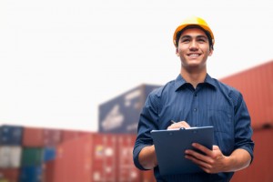 Smiling young engineer in a shipping yard examining cargo